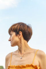 low-angle shot portrait of beautiful mature woman with short brown hair standing on river embankment in city of St. Petersburg and looking away in sun shining, enjoing summer. Copy space, vertical