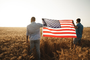 Two men patriots holding US flag above wheat field