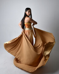 Full length portrait of pretty young asian woman wearing golden Arabian robes like a genie,...