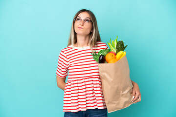 Young woman holding a grocery shopping bag isolated on blue background and looking up