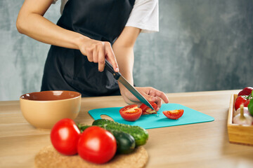 Woman in black apron on the kitchen cutting vegetables salad diet