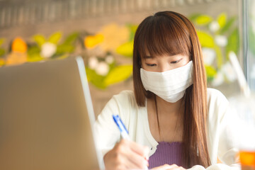 Young adult asian female with protective face mask work and study at cafe new normal lifestyle.