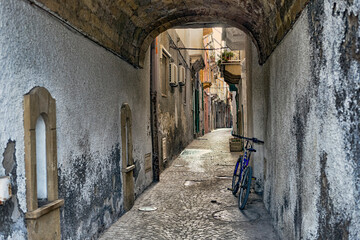 Suggestive glimpse of pedestrian route in ancient cobblestone  narrow alley between cracked and colored by time walls