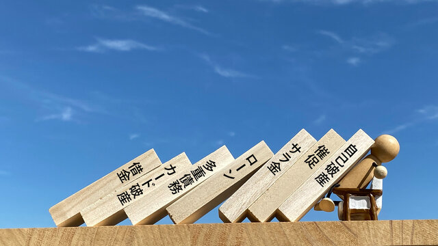 倒れるたくさんの板と前向きで受け止める人形_借金関連文字入り