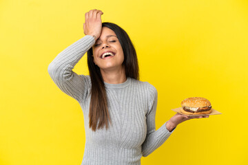 Young caucasian woman holding a burger isolated on yellow background has realized something and intending the solution