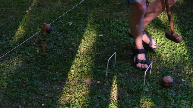 Person plays a sports game of croquet on a green field strike mallets on a ball and conducts through hoops.