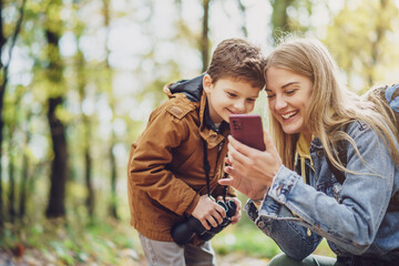 Happy mother and son are hiking in forest. They are using maps on smart phone.