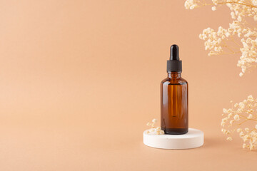Amber glass dropper bottle with black lid on white podium for product presentation on beige background with dry plants. Skincare products ,natural cosmetic. Beauty concept for face and body care