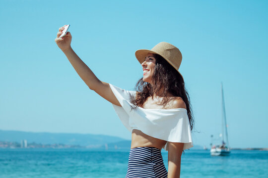 smiling woman in hat taking a selfie on the beach