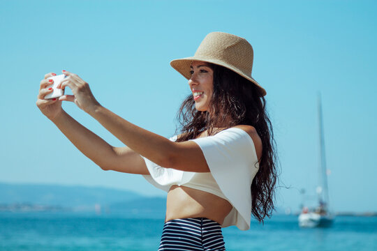 smiling woman in hat taking a selfie on the beach