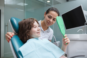 Obraz premium Adorable young boy checking teeth in the mirror after dental procedure at dentists office