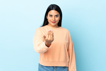 Young latin woman woman isolated on blue background inviting to come with hand. Happy that you came