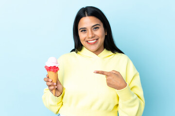 Young Colombian woman with a cornet ice cream isolated on blue background and pointing it