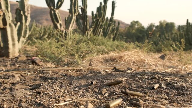Bullet casings falling to the ground in a cactus field in the desert. slow motion smoke coming out. Wild wild west cowboys scenery. Gun bullet shells flying in slow motion after being shot.
