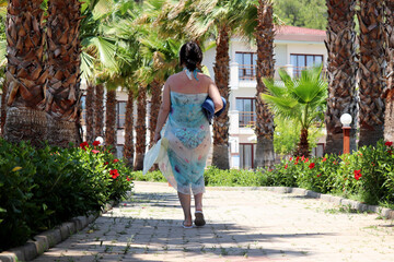 Vacation on tropical  resort. Woman in swimsuit and sarong walking on background of palm trees and...