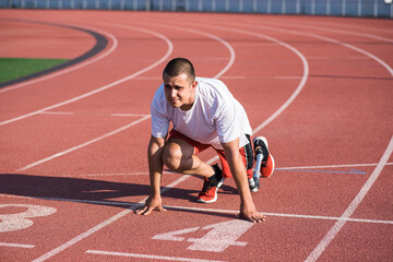 Caucasian male athlete with a prosthetic leg standing at the start on the track at the stadium. Sport concept.