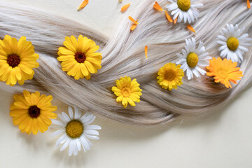 Chamomile and calendula flowers in blond hair. Pigtail.