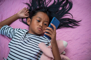 Asian girl watching content on her bed in the morning using a smartphone