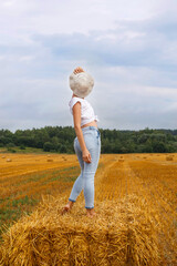 girl in straw hat stands on a haystack on a bale in the agricultural field after harvesting