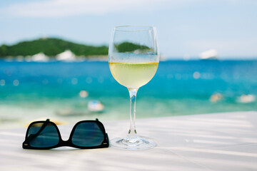 Glass of cold white wine and sunglasses with beach on background - Summer and travel vacation concept