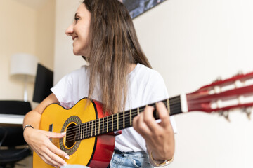 Fototapeta premium Attractive young female smiling while playing the guitar at home while learning new chords and practising new songs