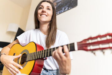 Attractive young female playing the guitar at home while learning new chords and practising new...