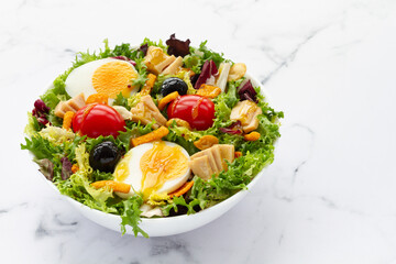 Salad with lettuce, egg, tuna, olives and honey and mustard vinaigrette on white background