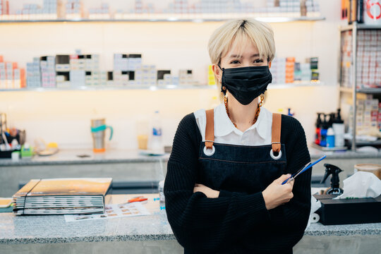 Asian female hairdresser wearing uniform and face mask on in barbershop during Coronavirus pandemic