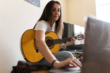 Attractive young female searching on the internet for tutorials to learn at home new chords and how to play the guitar