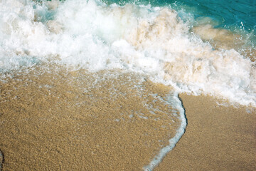 close up texture of the sea wave rolling on to the golden sandy beach. abstract nature background on a sunny summer day