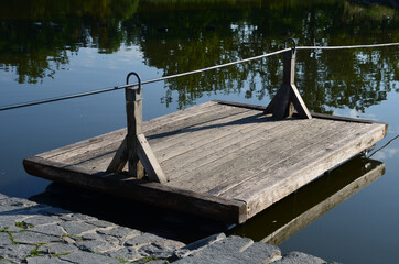 a wooden raft is tied to a taut rope. self-service ferry across the river, pond. People get on and...