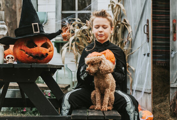 boy in a skeleton costume with a dog on the porch of a house decorated to celebrate a Halloween...