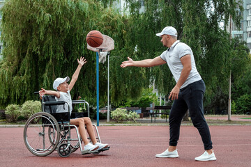 Dad plays with his disabled son on the sports ground. Concept wheelchair, disabled person, fulfilling life, father and son, activity, cheerfulness, basketball.