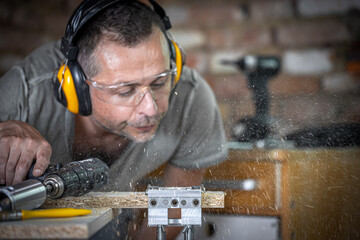 A male joiner blows wood off a board.