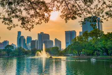 Lumphini park with beautiful lake with fountain and skyscrapers buildings on skyline at sunset....