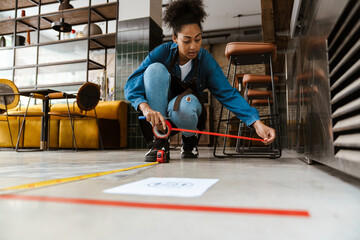 Black waitress in apron using tape measure while working at cafe