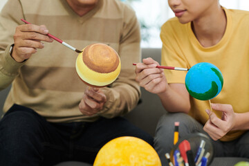 Father and son painting plastic balls when making solar system model for school