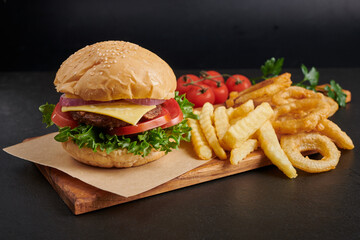 Homemade hamburger or burger with fresh vegetables and cheese lettuce and mayonnaise served, French fries on pieces of brown paper on black stone table . concept of fast food and junk food