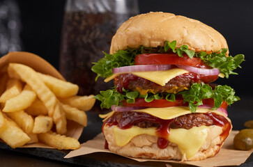 Homemade hamburger or burger with fresh vegetables and cheese lettuce and mayonnaise served, French fries on pieces of brown paper on black stone table . concept of fast food and junk food