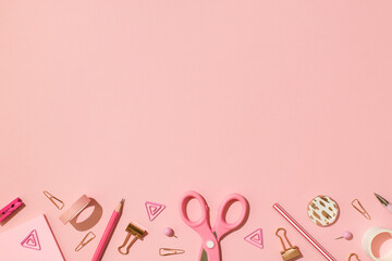 Overhead photo of school equipment scissors tape paper clips pins pencil pen and spirals isolated on the pink backdrop with empty space