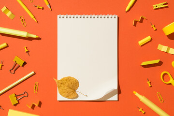 Top view photo of yellow autumn leaf on open spiral notepad with curled corner and school supplies...