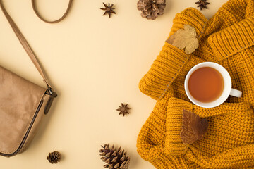 Top view photo of leather bag cup of tea autumn brown leaves yellow sweater anise and pine cones on isolated pastel orange background with copyspace