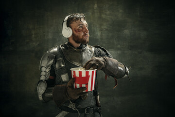 Portrait of one brutal bearded man, medeival warrior or knight in headphones with bucket of popcorn...