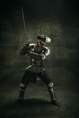 Portrait of one brutal bearded man, medeival warrior or knight in VR glasses with sword over dark...