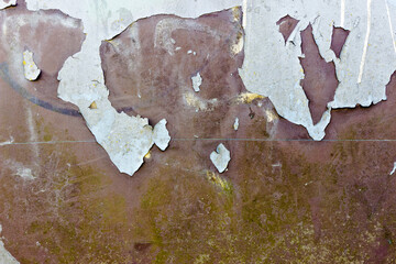Light grey paint peels of a brown metal surface