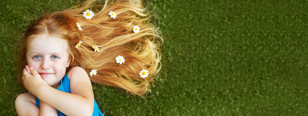 portrait of a beautiful little girl with healthy red hair with chamomile flowers lying on the grass