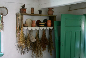 An interior of an old rural hose with all the neccesary items located on shelves, including brooms, pots, cauldrons, cuttlery, and bowls see next to green wooden door on a sunny summer day in Poland