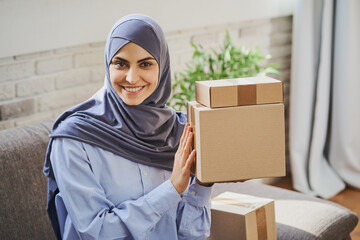 Pretty Arabian woman holding few carboard boxes and giving a broad smile