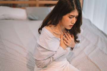 Portrait of 20s young Asian woman having difficulty breathing in bedroom at night. Shortness of...