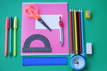 Pink notebook with stationery accessories on a green background. 1 September is the day of knowledge.